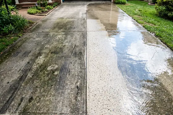 A concrete driveway mid-wash, with a sharp line between the dirty grey half and the clean pale half.