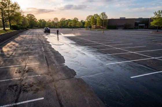 An empty commercial parking lot being washed, bright white stall lines against clean asphalt.